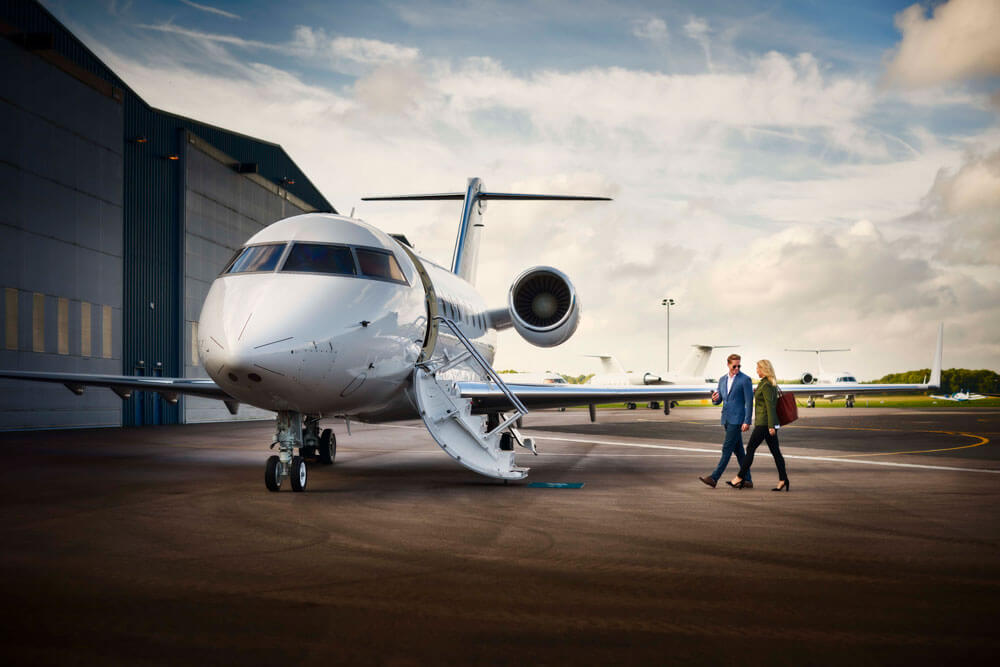 2 people walking on a runway to a luxury private jet outside a hangar booked by Dela World Charter.