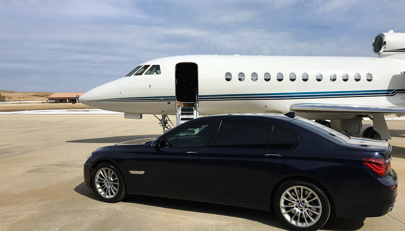 A luxury bmw car parked on a runway next to a private jet booked by Dela World Charter.