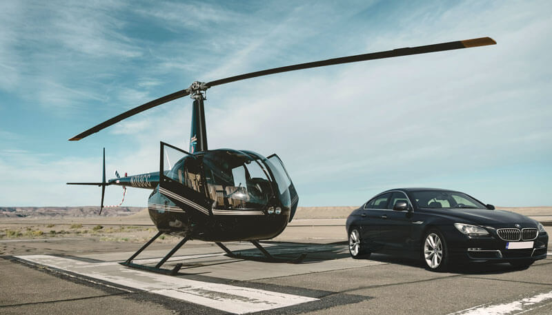 A luxury bmw car parked on a runway next to a helicopter booked by Dela World Charter.