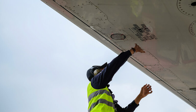 An airport worker carries out maintenance on the wing of a grounded aircraft.